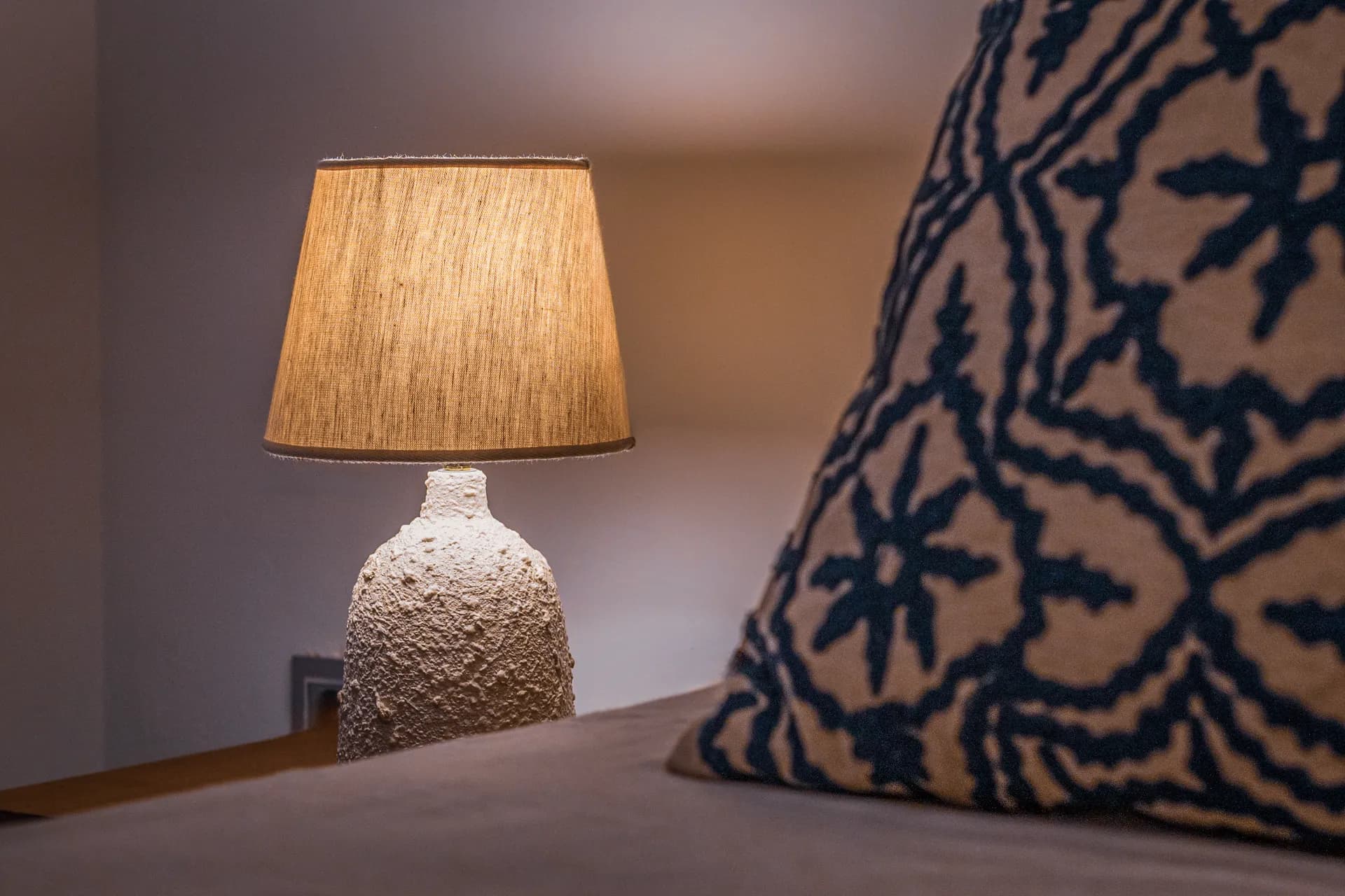 Détail décoratif d'une chambre Nautilus : lampe artisanale et coussin brodé bleu