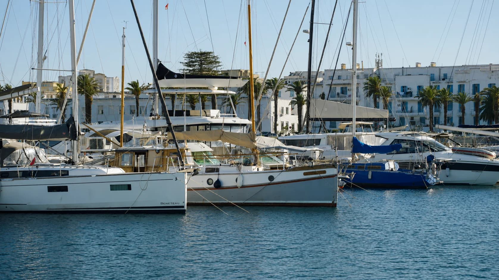 Voiliers et yachts amarrés le long des pontons de Marina Bizerte, ville blanche et palmiers en arrière-plan